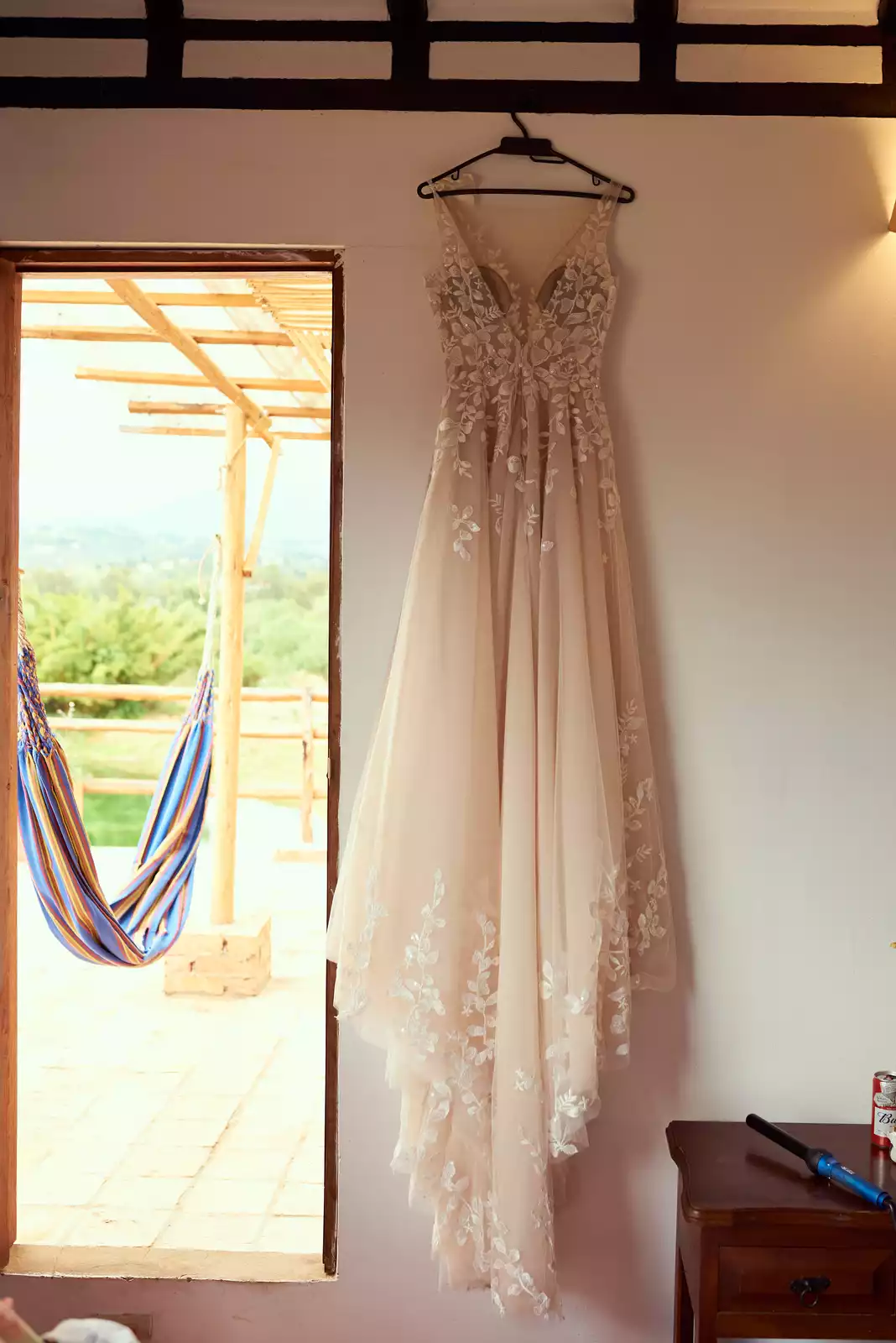 Vestido de novia colgado frente a una ventana con vista al jardín en Ave María